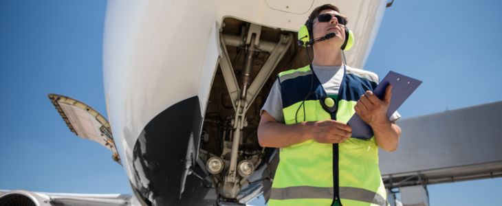 an airline employee in a vest standing underneath an airplane