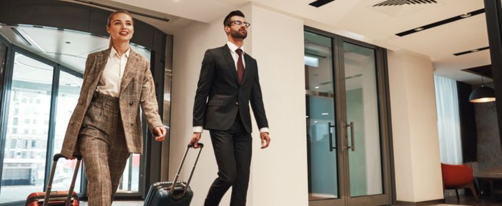 a businessman and businesswoman walking with suitcases into a hotel lobby